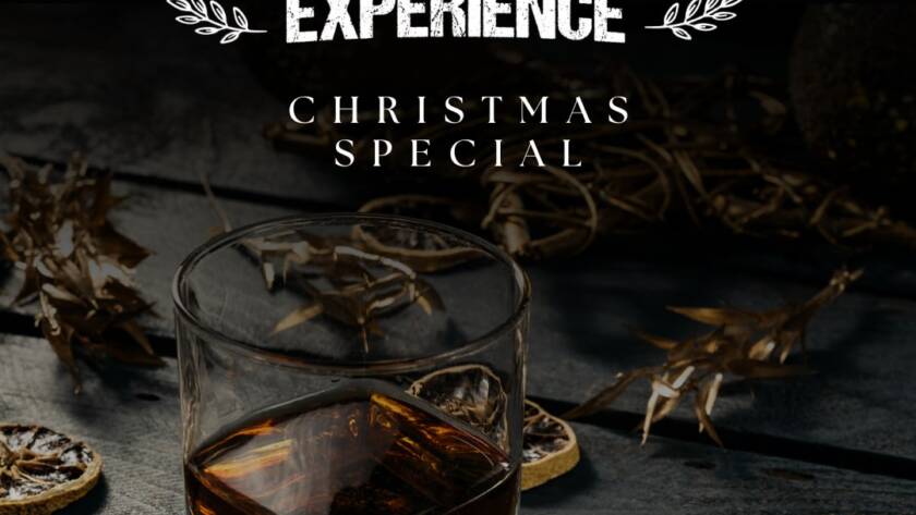 A glass of whiskey sits on a wooden table adorned with dried leaves and citrus slices. Bold white text above reads "Tour & Whiskey Tasting Experience" and "Christmas Special." The image has a dark, rustic ambiance.